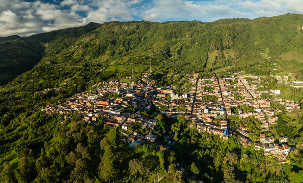 Aerial view of a vibrant town nestled amidst rolling green hills, a tapestry of terracotta roofs contrasting with the lush vegetation, Tamesis, Antioquia, Colombia.