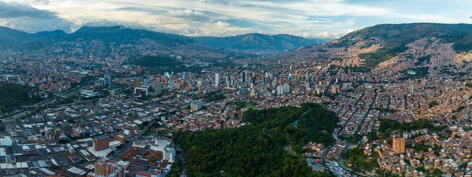 Aerial view of a vast cityscape nestled amongst rolling green mountains under a soft sky, Medellin, Antioquia, Colombia.