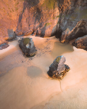 Aerial view of sunlight kissing the rugged cliffs and soft sands, painting a serene coastal scene, Vila do Bispo, Faro District, Portugal.
