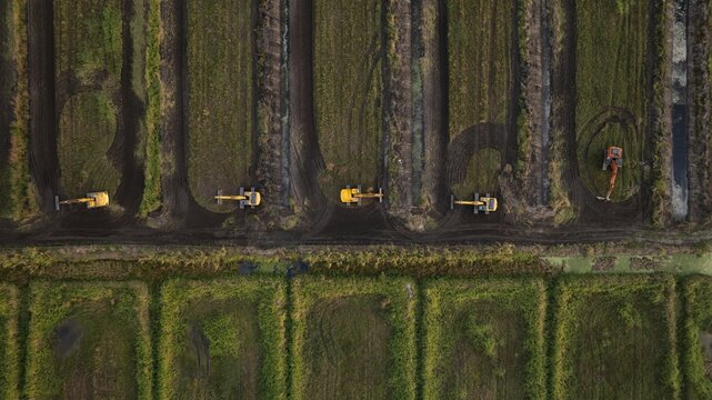 Aerial view of heavy machinery carving deep, dark furrows into the earth under a golden light, textures of soil and metal contrasting sharply, West Palm Beach, Florida, United States.
