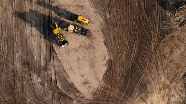 Aerial view of yellow earthmovers carving paths in the ochre-toned earth, their shadows stretching long across the construction site, West Palm Beach, Florida, United States.