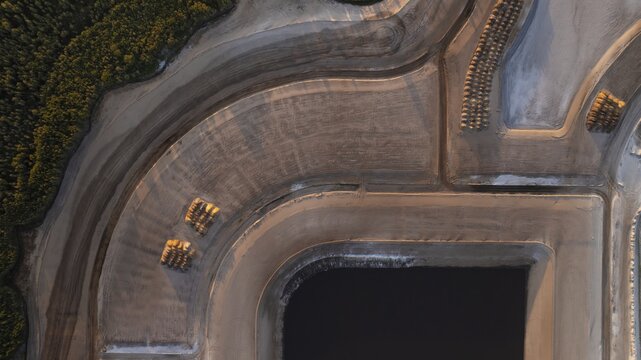 Aerial view of curving earthworks and dark water, a study in texture and tone, contrasted with the green of nearby trees, West Palm Beach, Florida, United States.
