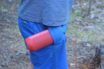 A single red plastic electronic mobile music speaker lies in a man's blue trouser pocket on a summer street