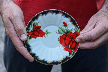 the man hands are holding one white empty ceramic plate with a pattern of red flowers 