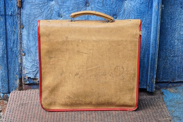 one old brown leather schoolbag standing on the floor near the blue wall on the street