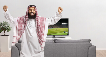Excited arab man in traditional clothing watching football and cheering