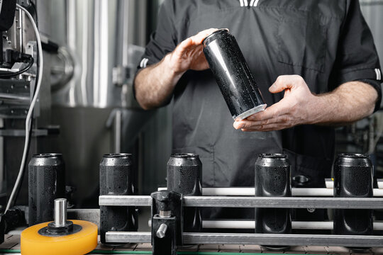 Worker man inspecting craft beer cans in modern brewery factory