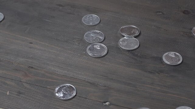 Loose coins fall by hand onto a wooden table