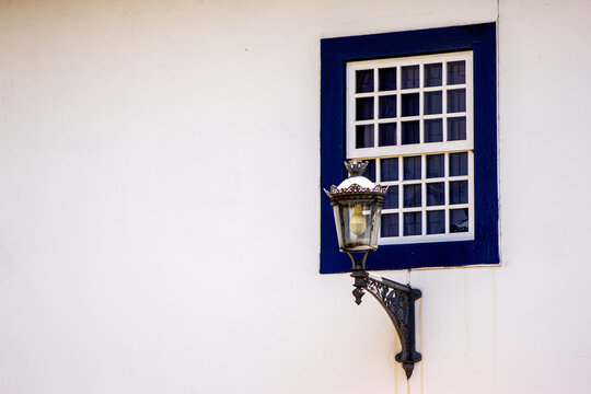 Janela com formas geom&eacute;tricas em parede banca com vinheta de cor azul e l&acirc;mpada de constru&ccedil;&atilde;o antiga. 