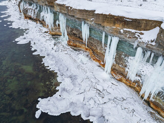 Aerial drone view of frozen Pakri cliff in Paldiski, Estonia, featuring massive ice formations, icicles, and snow-covered limestone rocks.
