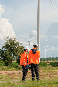 Engineer team standing near wind turbine carrying maintenance equipment reviewing renewable energy task promoting sustainable electric generation teamwork innovation outdoor green technology project