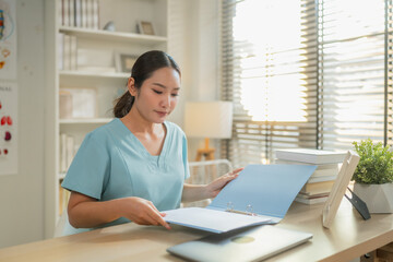 Naklejka na ściany i meble Female healthcare professional reviewing medical documents at desk with laptop in clinic office, administrative medical workflow, patient record management and modern healthcare documentation concept.