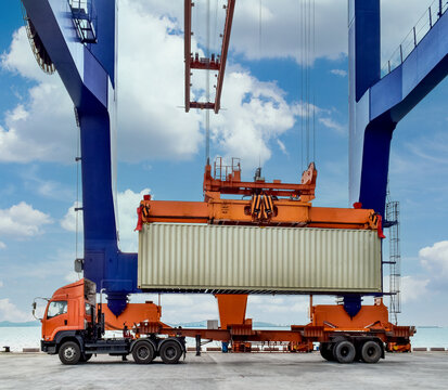 Side view of a massive quay crane loading a shipping container onto a heavy-duty truck at a port terminal.