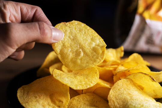 Intimate photograph capturing fingers clutching crispy salted delicacy under warm lighting