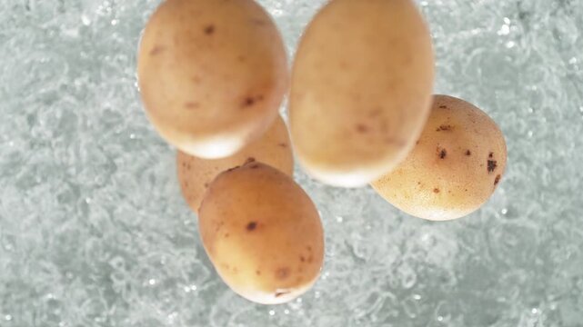 Unpeeled Potatoes Falling Into A Pot Of Boiling Water Making A Splash in Slow Motion, Table Top View