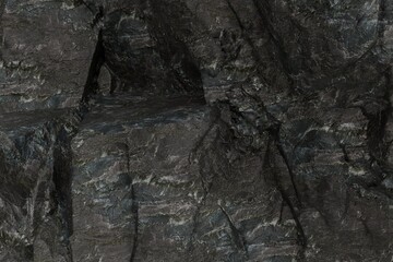A rugged, dark grey and black rock face dominates the frame, showcasing deeply textured layers, cracks, and shadowy crevices. Natural, weathered stone