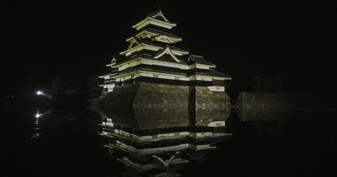 Glowing, ancient 16th century Matsumoto castle reflecting in water of moat at night