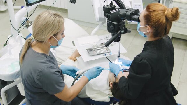 Dental staff conduct patient treatment at a clinic using a microscope for precision during a checkup visit to ensure dental health