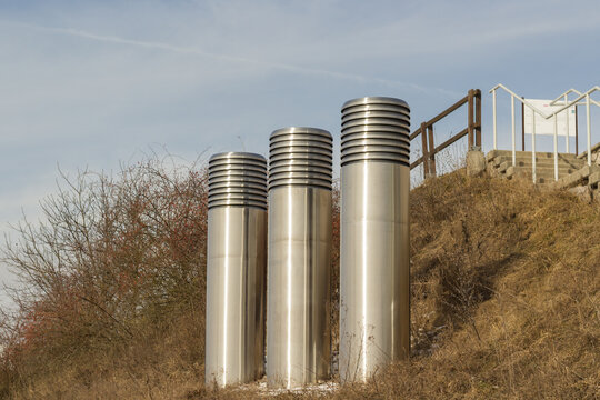 Trzy stalowe czerpnie terenowe na skarpie przy ogrodzeniu &ndash; instalacja wentylacyjna, doprowadzenie powietrza i infrastruktura techniczna.