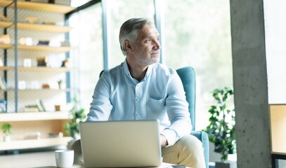 Smiling businessman sitting in office lobby working on laptop. Male business professional working...