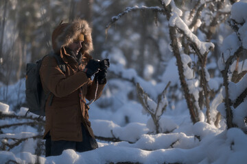 A man with a camera takes pictures in an atmospheric winter snow-covered forest.