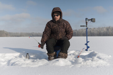 A fisherman ice fishing on a frozen lake on a sunny winter day