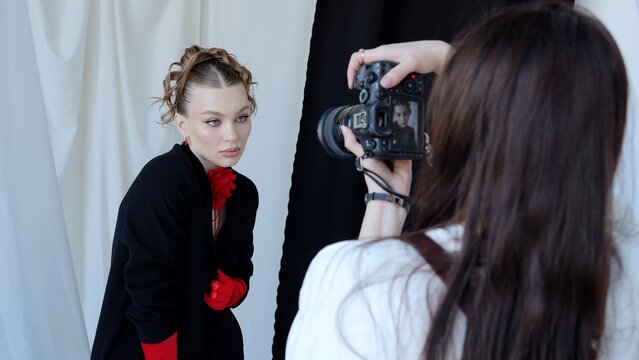 Professional photographer using digital camera while shooting fashion model, creating elegant studio portrait with dramatic lighting and dynamic pose