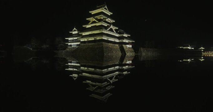 Yellow glow coming from ancient 16th century Matsumoto castle as it casts reflection in moat - wide shot