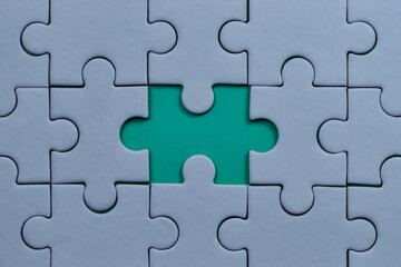 Gray jigsaw puzzle with a single missing piece revealing turquoise background