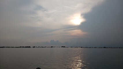 Time-lapse clouds drift over a serene river and lake at sunset as the orange sun reflects off the water, creating a beautiful nature landscape during a summer evening travel dusk © asrafulshafin