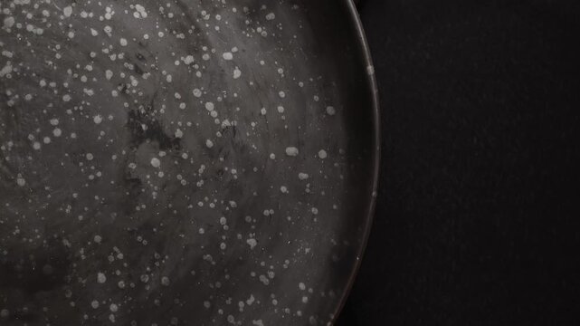 A round metal plate rests on black fabric, showing a speckled pattern. The plate has a unique surface texture.