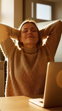 Woman stretches at desk with laptop in sunny home office during break. Female worker relaxes with laptop nearby. Woman takes break stretching at desk. Relaxed stretching in home office with laptop.