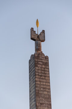 View of a tall, aged stone obelisk crowned with a golden spire reaching towards the pale blue sky, a silent sentinel, Yerevan, Yerevan, Armenia.