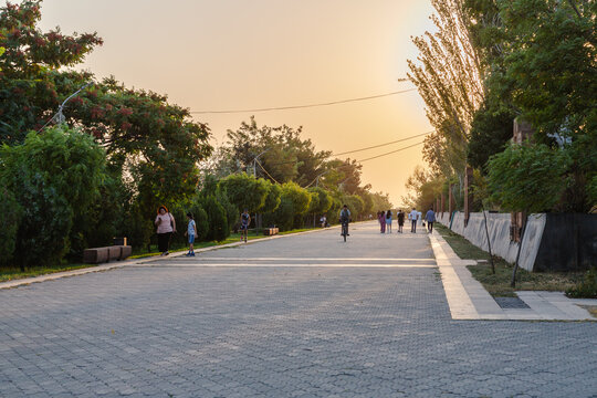 Yerevan, Armenia - 26 August 2025: View of a sunlit pathway lined with vibrant trees and strolling figures, casting soft shadows on the textured stone, evoking a tranquil urban escape.