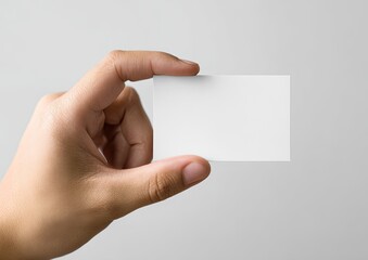 Obraz premium A hand holds a blank rectangular card, angled against a plain gray background