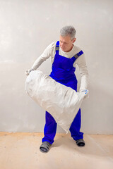 Vertical view a man carries construction debris in a white bag.