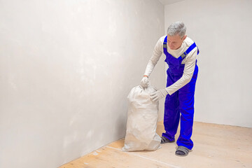 A man is carrying construction debris in a white bag.