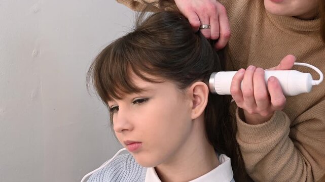 Trichologist examines hair and scalp of young woman in salon using trichoscope and dermatoscope. Woman's hair loss, dandruff and oily hair problems, scalp treatment and hair care consultations