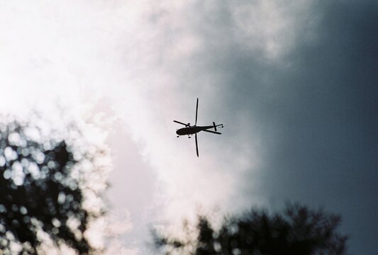 Silhouette of a transport helicopter flying against a bright sky, analog photography