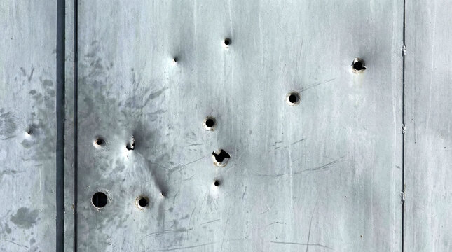 Bullet holes in metal door with weathered surface showing texture and damage. Close-up of bullet holes creates a stark visual narrative highlighting impact and destruction.