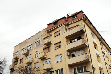 Fototapeta premium Aged residential apartment building with peeling facade and balconies in Sombor, Serbia. Urban housing, renovation and real estate concept in Eastern Europe.