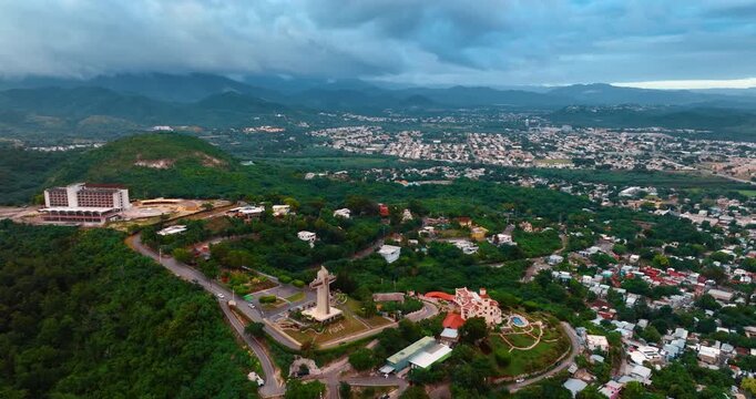 Vast green cityscape of Ponce, Puerto Rico. Approaching the Cross Monument on the hill. Dramatic clouds covered the horizon. Aerial view.