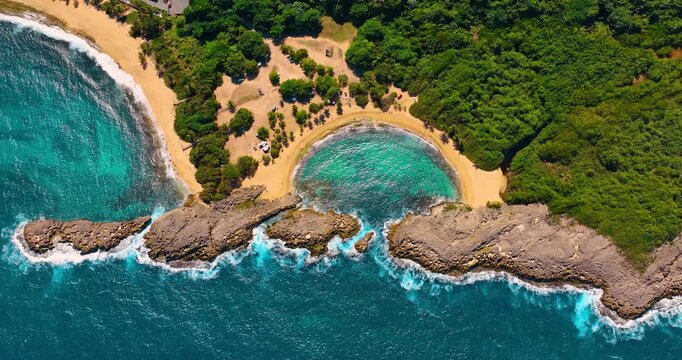Beautiful turquoise water splashes to the sandy beach. Lush greenery grows on the shore. Manati Beach in Puerto Rico. Top view.