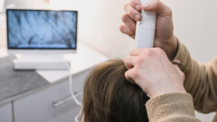 Trichologist examines hair and scalp of young woman in salon using trichoscope and dermatoscope....
