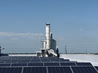 Obraz premium Wide shot of an industrial rooftop featuring rows of solar panels and a large vertical air scrubber system with exhaust stacks. This sustainable facility represents green energy integration, environme