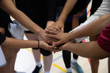 Diverse team placing stacked hands together on gym floor, revealing sneakers and painted lines