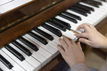 Fototapeta premium Child's Hands Playing Piano Keys on a Vintage Wooden Musical Instrument