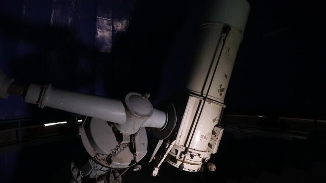 A slow upward pan reveals a large, rusted, and abandoned telescope inside a dark, decaying observatory dome. Sunlight peeks through a narrow opening in the deep blue ceiling.