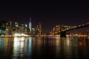 New York City skyline at night with Brooklyn Bridge and river reflections