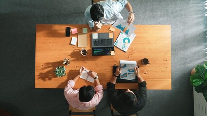 Fototapeta na wymiar Top aerial view of caucasian business people sharing idea and writing report. Professional diverse people working together and brainstorming marketing plan at meeting table with graph. Convocation.